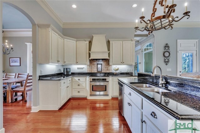 kitchen with sink, hanging light fixtures, light hardwood / wood-style flooring, custom range hood, and stainless steel appliances