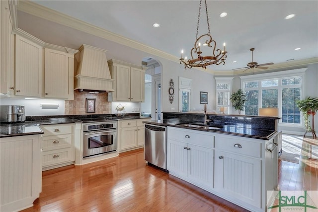 kitchen with sink, custom exhaust hood, ornamental molding, appliances with stainless steel finishes, and pendant lighting