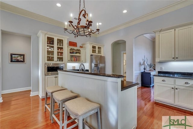 kitchen with hanging light fixtures, light wood-type flooring, ornamental molding, an island with sink, and stainless steel appliances