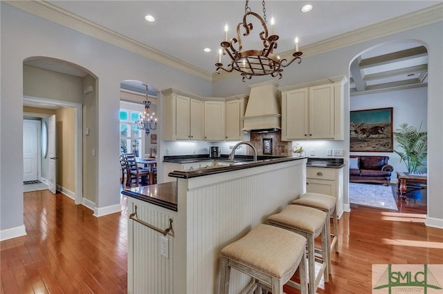 kitchen featuring decorative light fixtures, custom exhaust hood, a notable chandelier, light hardwood / wood-style floors, and cream cabinetry