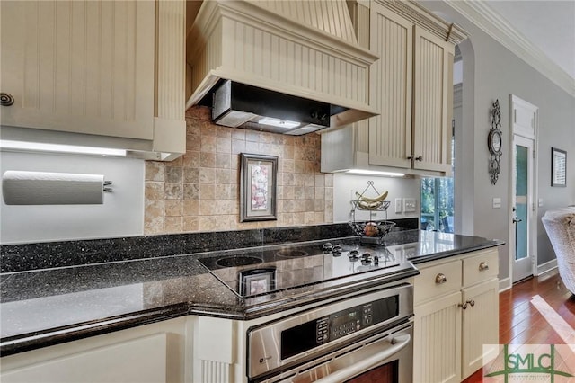 kitchen with stovetop, stainless steel oven, ornamental molding, custom range hood, and cream cabinetry