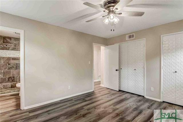 unfurnished bedroom with ceiling fan, dark hardwood / wood-style flooring, ensuite bath, and two closets