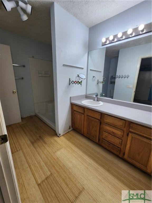 bathroom featuring hardwood / wood-style flooring, vanity, a textured ceiling, and walk in shower