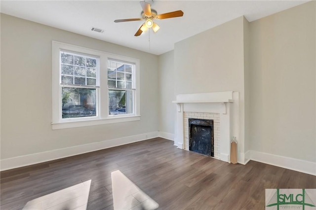 unfurnished living room featuring a brick fireplace, dark wood-type flooring, and ceiling fan