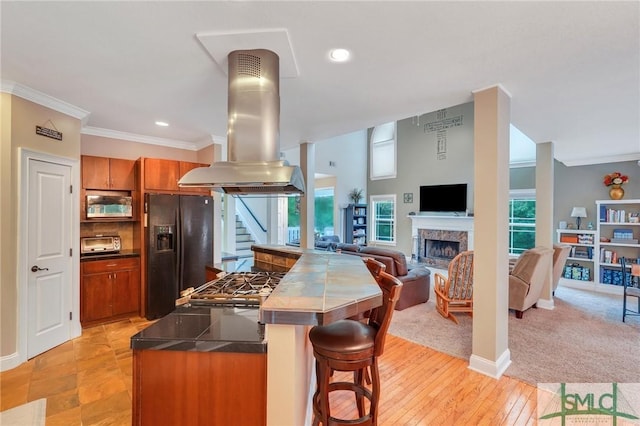 kitchen with a kitchen bar, black fridge with ice dispenser, island range hood, light carpet, and ornamental molding