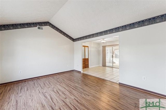 unfurnished room featuring vaulted ceiling, a textured ceiling, and light wood-type flooring