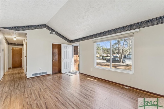 interior space featuring hardwood / wood-style floors, vaulted ceiling, and a textured ceiling