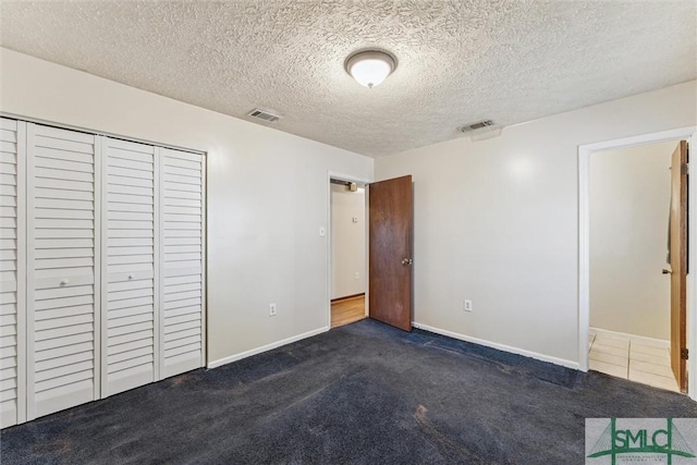 unfurnished bedroom featuring dark carpet, a closet, and a textured ceiling