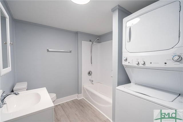 full bathroom featuring toilet, baseboards, bathing tub / shower combination, wood finished floors, and stacked washer and clothes dryer