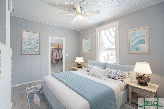 bedroom featuring a ceiling fan, baseboards, wood finished floors, a spacious closet, and a closet