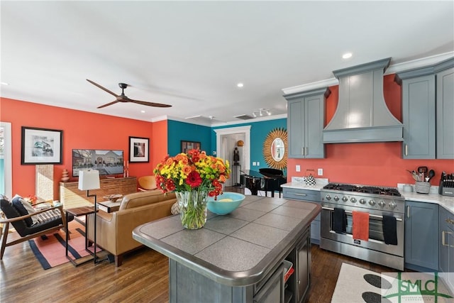 kitchen featuring stainless steel stove, ceiling fan, tile counters, dark hardwood / wood-style flooring, and custom exhaust hood