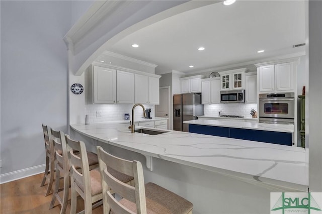 kitchen featuring sink, hardwood / wood-style floors, stainless steel appliances, white cabinets, and decorative backsplash