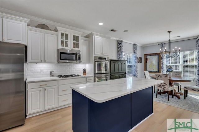 kitchen with white cabinetry, crown molding, decorative light fixtures, appliances with stainless steel finishes, and a kitchen island