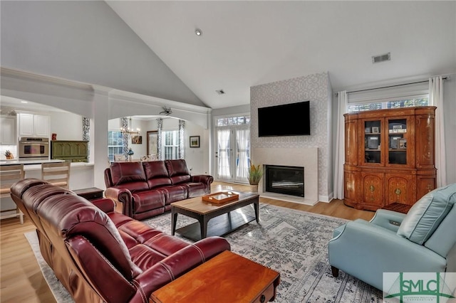 living room with a large fireplace, high vaulted ceiling, light hardwood / wood-style floors, and a notable chandelier