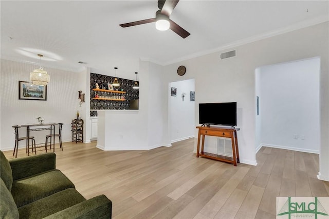 living room featuring crown molding, light hardwood / wood-style flooring, ceiling fan, and indoor bar