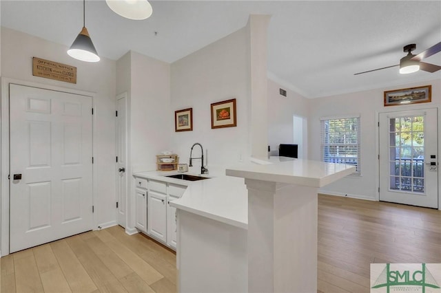 kitchen with white cabinetry, sink, hanging light fixtures, kitchen peninsula, and light wood-type flooring