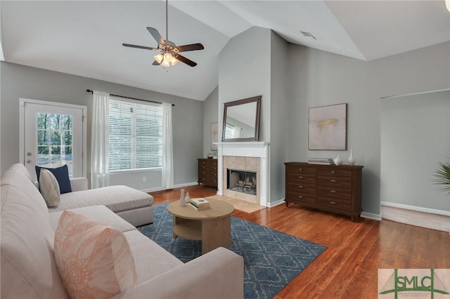 living room with a tiled fireplace, wood-type flooring, lofted ceiling, and ceiling fan