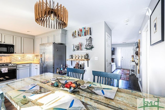 kitchen with gray cabinets, backsplash, light stone counters, stainless steel appliances, and dark wood-type flooring