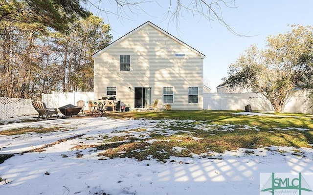 snow covered rear of property featuring a lawn and an outdoor fire pit