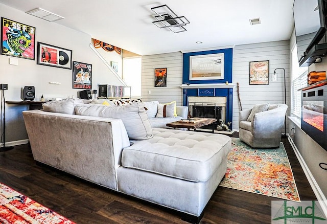 living room with dark wood-type flooring, wooden walls, and a tiled fireplace