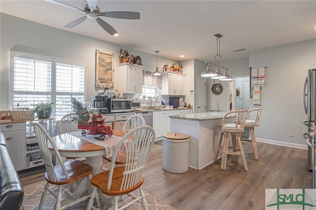 kitchen with plenty of natural light, white cabinetry, hanging light fixtures, a center island, and light stone countertops