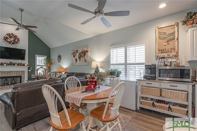 dining area featuring ceiling fan, lofted ceiling, a fireplace, and light wood-type flooring