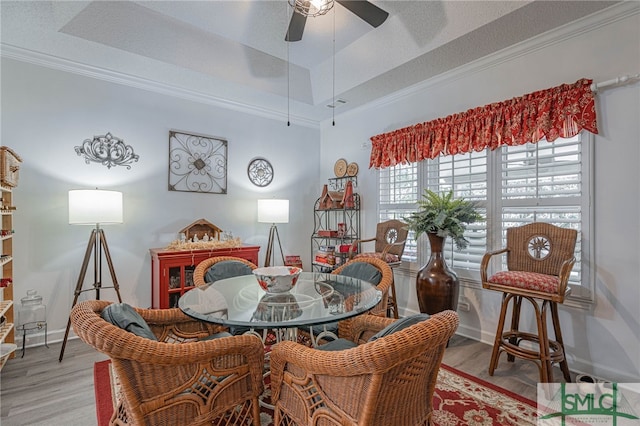 dining room featuring vaulted ceiling, ceiling fan, a tray ceiling, crown molding, and light hardwood / wood-style flooring