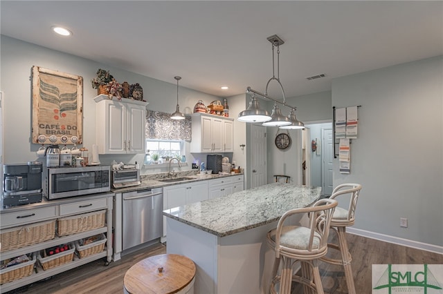 kitchen featuring white cabinetry, a center island, appliances with stainless steel finishes, pendant lighting, and light stone countertops