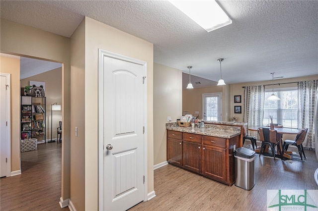 kitchen featuring pendant lighting, a textured ceiling, light stone counters, and light hardwood / wood-style flooring