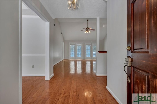 entrance foyer featuring light wood finished floors, baseboards, lofted ceiling, ceiling fan with notable chandelier, and a textured ceiling