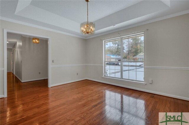 spare room featuring hardwood / wood-style flooring, ornamental molding, a chandelier, and a tray ceiling