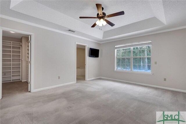 empty room featuring ceiling fan, a tray ceiling, ornamental molding, a textured ceiling, and light carpet