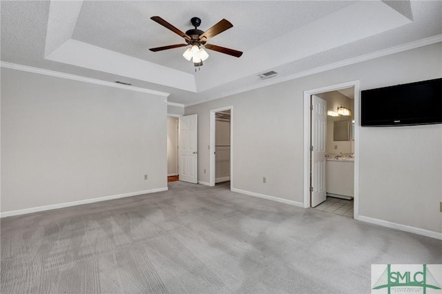 unfurnished bedroom with ceiling fan, ensuite bath, a tray ceiling, and a spacious closet