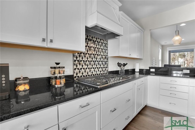 kitchen featuring wood-type flooring, custom range hood, white cabinets, dark stone counters, and stainless steel gas stovetop