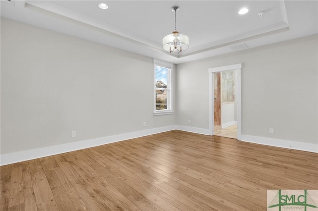 unfurnished room with a notable chandelier, light hardwood / wood-style floors, and a raised ceiling