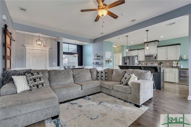 living room featuring wine cooler, ceiling fan, a barn door, and hardwood / wood-style floors