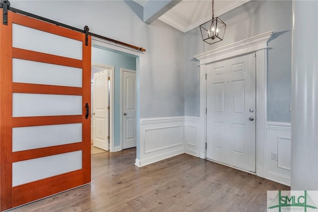 foyer entrance featuring hardwood / wood-style flooring, ornamental molding, a barn door, and a notable chandelier