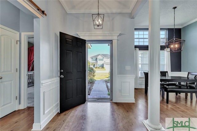 entryway with a textured ceiling, ornamental molding, a notable chandelier, a barn door, and hardwood / wood-style floors