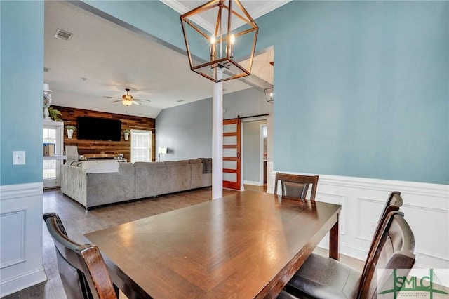 dining area with ceiling fan with notable chandelier, wooden walls, and a barn door