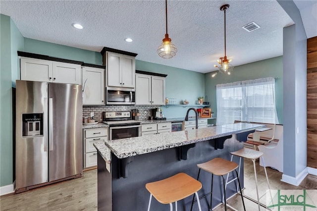 kitchen featuring pendant lighting, stainless steel appliances, a textured ceiling, a center island with sink, and decorative backsplash