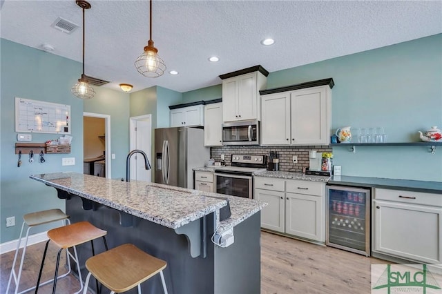 kitchen featuring appliances with stainless steel finishes, wine cooler, a textured ceiling, and decorative light fixtures