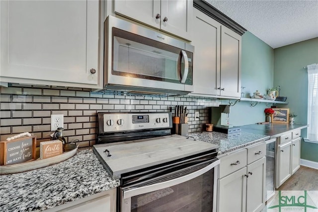 kitchen featuring white cabinetry, light stone counters, stainless steel appliances, a textured ceiling, and light wood-type flooring