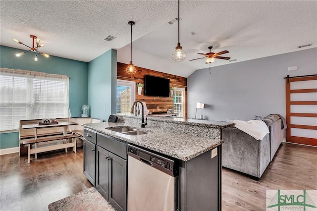 kitchen featuring decorative light fixtures, wood walls, dishwasher, sink, and a center island with sink