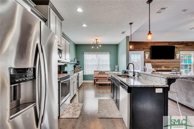 kitchen featuring sink, light stone counters, appliances with stainless steel finishes, wooden walls, and pendant lighting