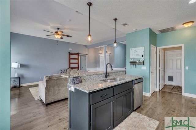 kitchen with decorative light fixtures, dishwasher, sink, a barn door, and a center island with sink