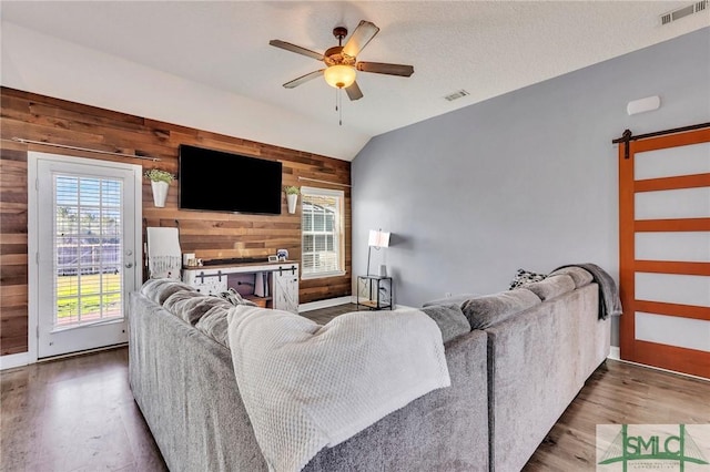 living room with a fireplace, wood walls, vaulted ceiling, ceiling fan, and a barn door