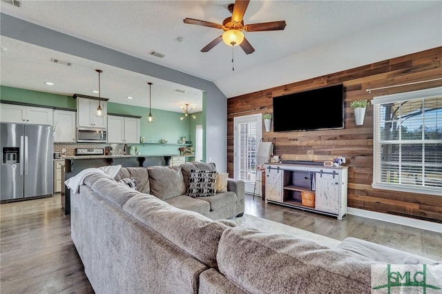 living room featuring lofted ceiling, ceiling fan, wood-type flooring, a textured ceiling, and wood walls