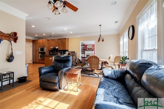 living room featuring ornamental molding, a fireplace, ceiling fan, and light hardwood / wood-style flooring