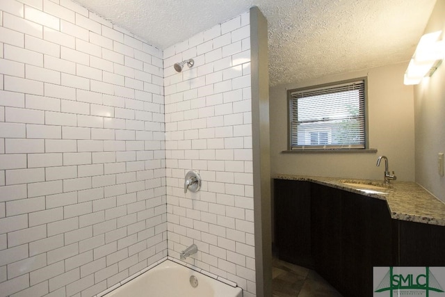 bathroom with vanity, a textured ceiling, and tiled shower / bath