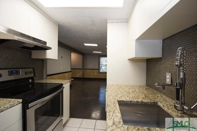 kitchen featuring stainless steel range with electric stovetop, light stone countertops, light tile patterned floors, and white cabinets